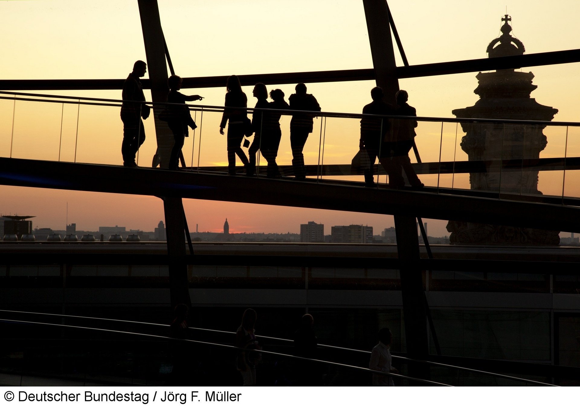 Brücke des Bundestags vor gelbem Himmel mit schattigen Silouhetten von Besuchern