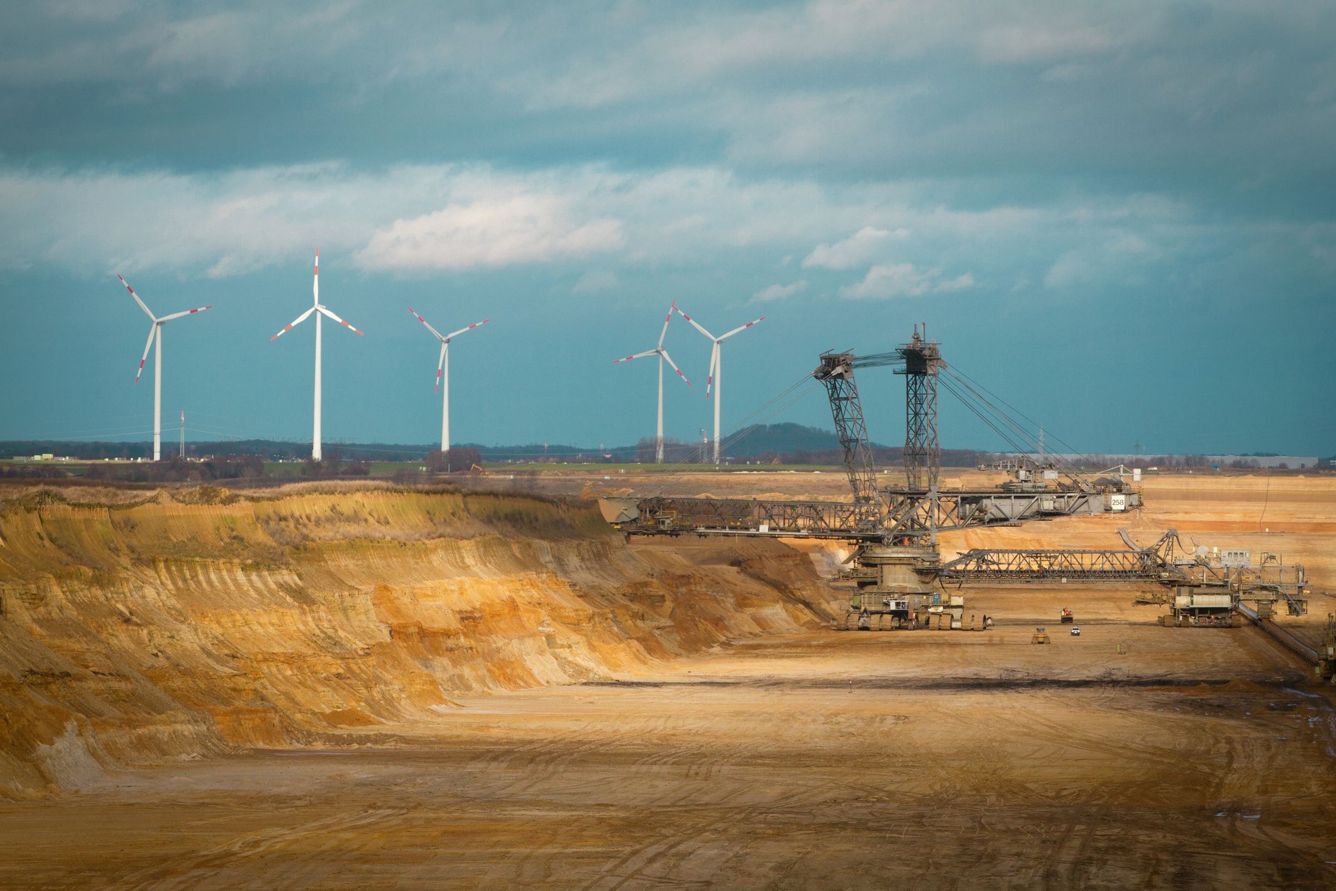 Kohlegrube mit Windrädern am Horizont vor wolkenbehangenem Himmel