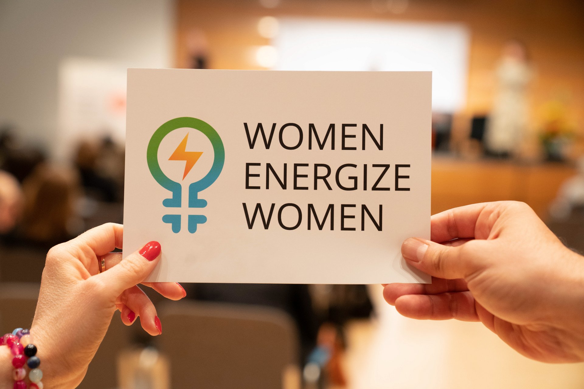 Schild mit Women Energize Women Logo wird hochgehalten 