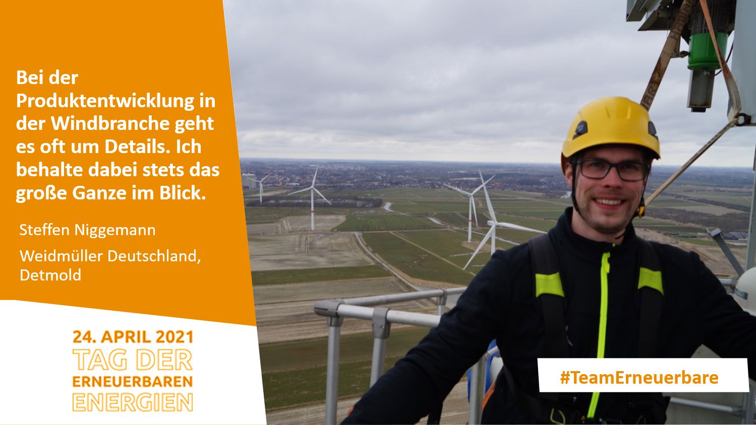 Mann mit Helm und Kletterausrüstung steht vor einem Windpark