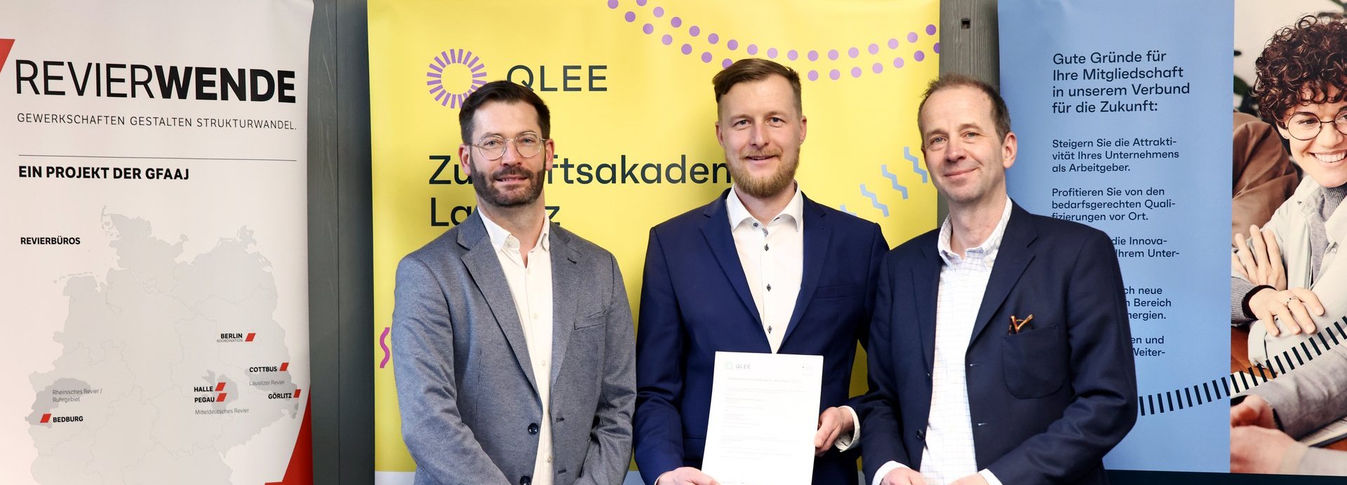 Beschreibung: Drei Mitarbeitende stehen nebeneinander und einer hält den unterschriebenen Vertrag