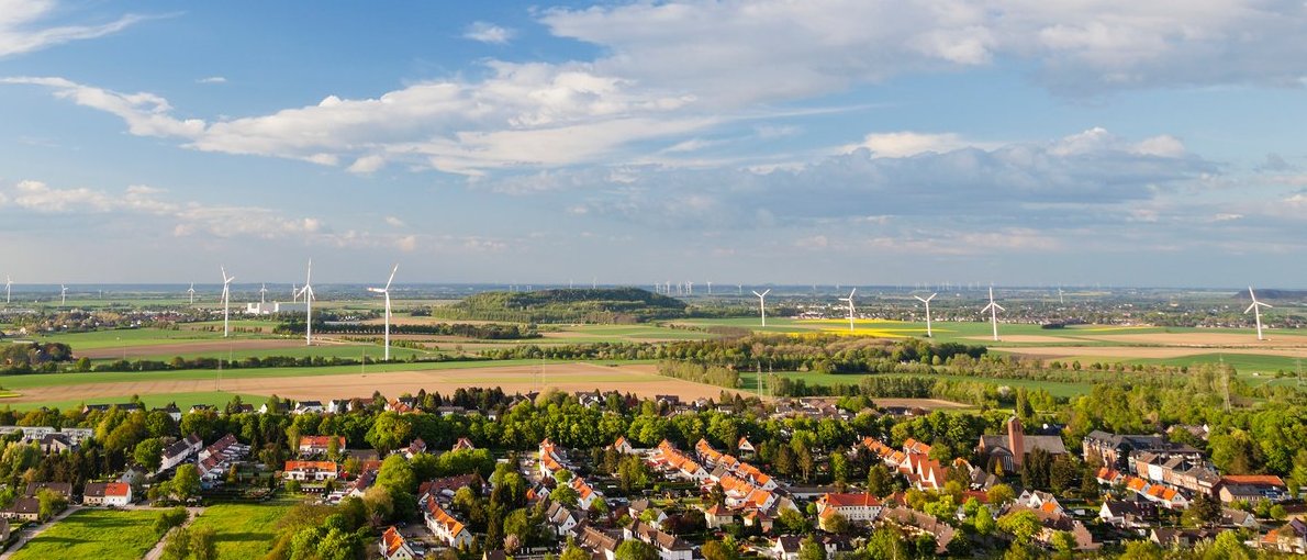 Landschaft mit Häusern, Windrädern und blauem Himmel