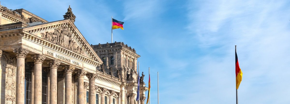 Bundestagsgebäude mit zwei deutschen Flaggen vor bewölktem blauem Himmel