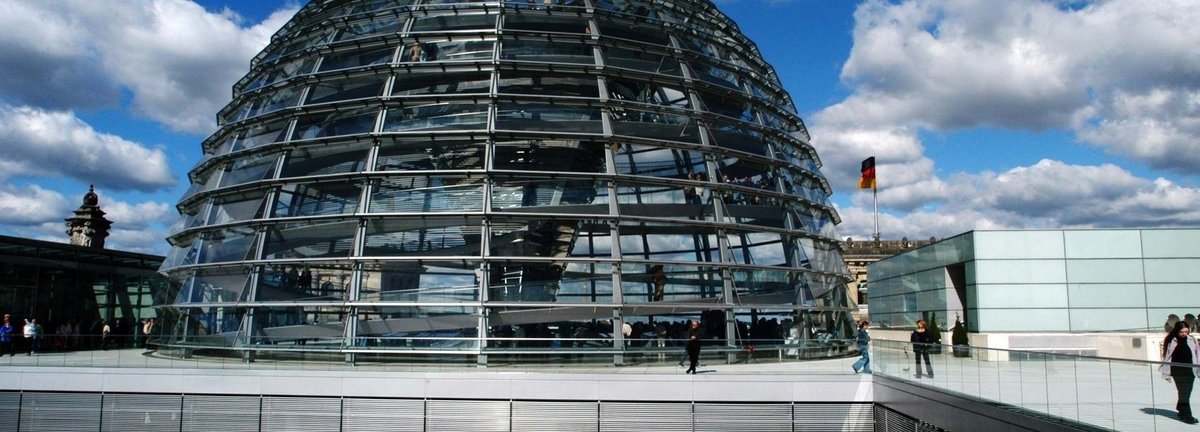 Die Glaskuppel des deutschen Bundestages vor einem leicht bewölkten dunkelblauem Himmel