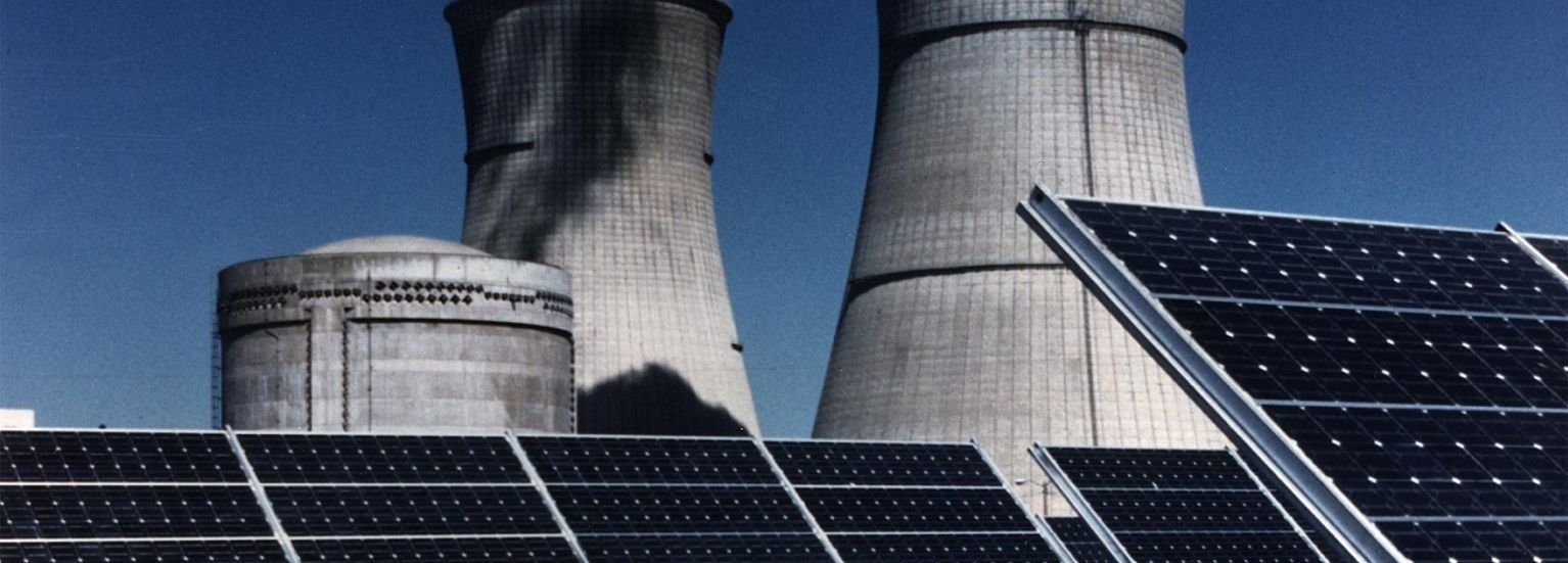 Solarkollektoren im Vordergrund mit Kraftwerksschornsteinen im Hintergrund vor dunkelblauem Himmel