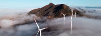 Luftaufnahme von einer Drohne eines Windparks über den Wolken mit einem Berg im Hintergrund und blauem Himmel