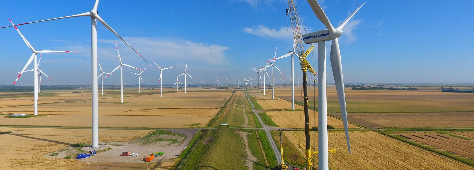 Beschreibung: Viele Windräder auf Feldern, an denen ein Kran arbeitet