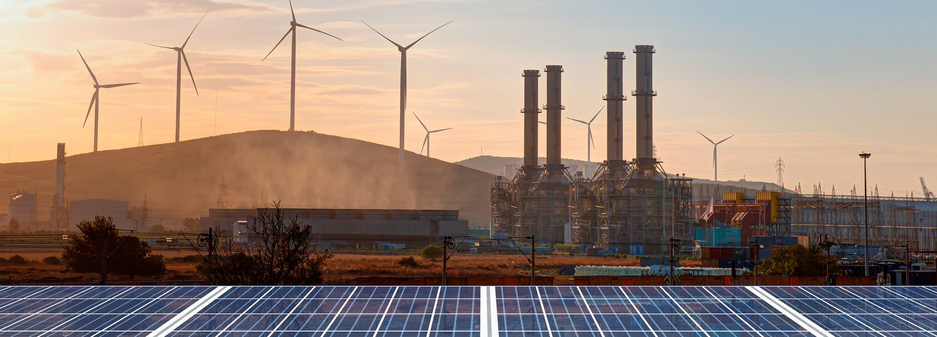 Beschreibung: Solarpanele im Vordergrund mit Windrädern im Hintergrund und einem Sonnenuntergang