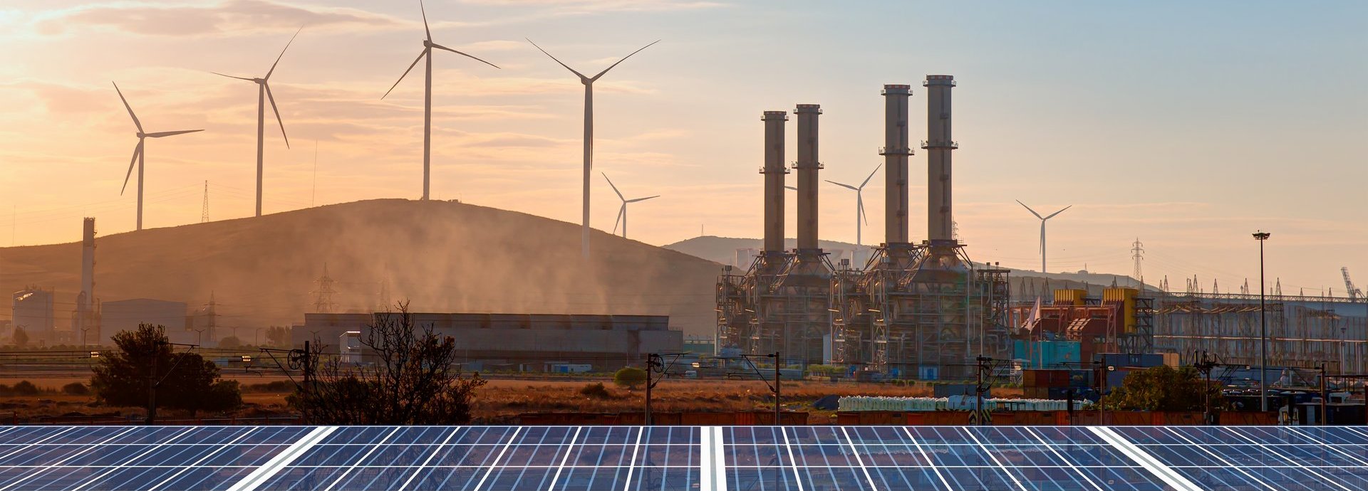 Beschreibung: Solarpanele im Vordergrund mit Windrädern im Hintergrund und einem Sonnenuntergang