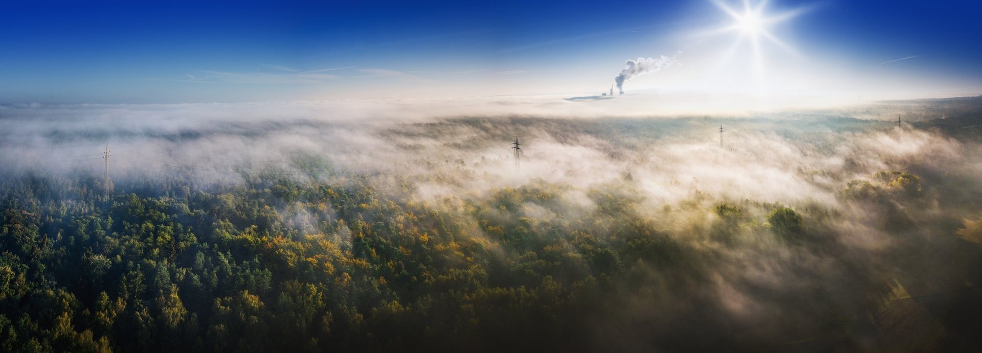 Beschreibung: Luftaufnahme über waldige Landschaft mit Industrieabgasen im Hintergrund