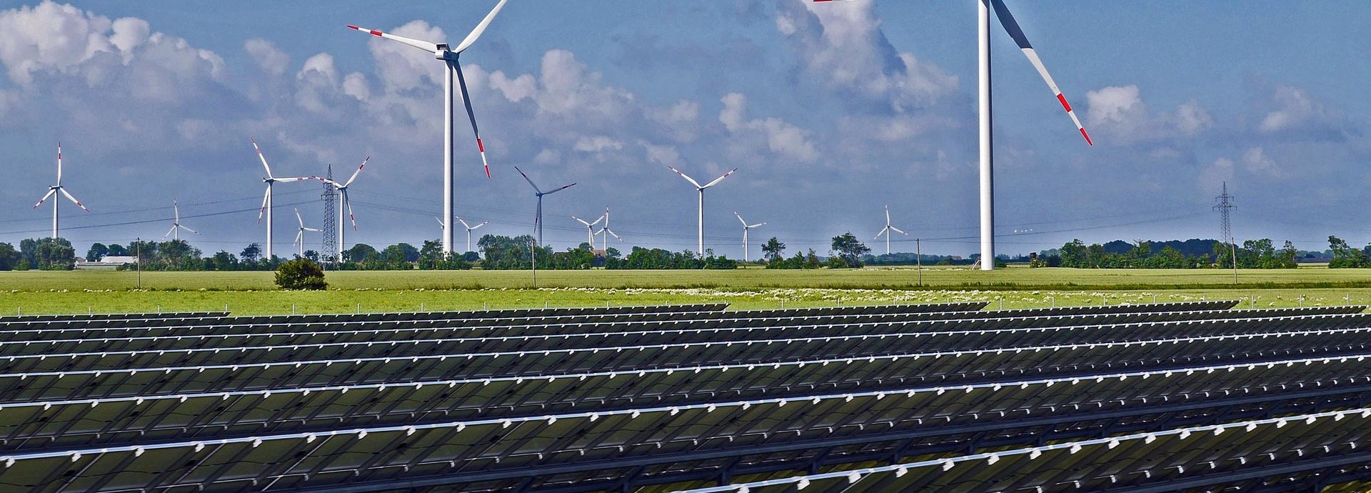 Solarpark mit Solarkollektoren auf einer Wiese und Windrändern im Hintergrund