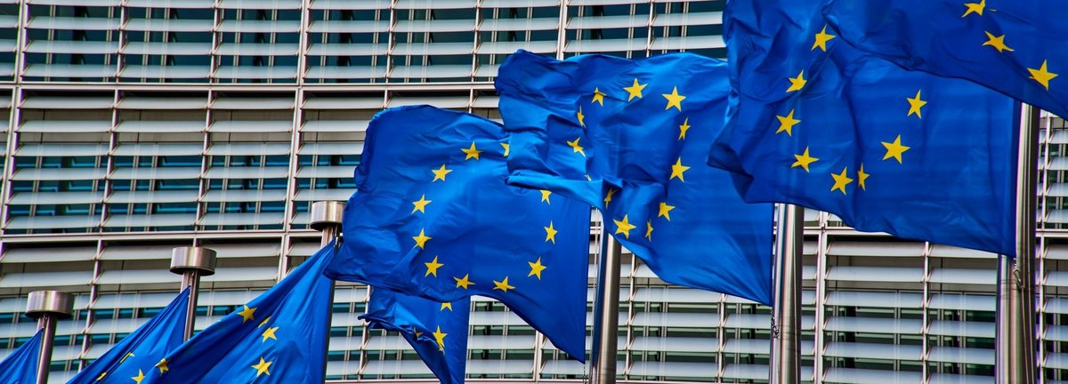 Nahaufnahme des Gebäudes der Europäischen Kommission in Brüssel, davor wehende EU Fahnen