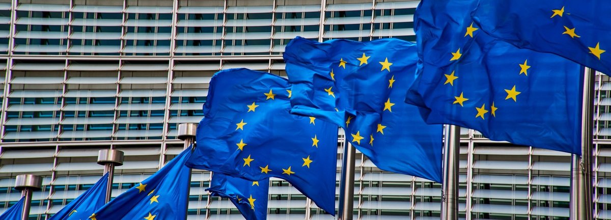 Nahaufnahme des Gebäudes der Europäischen Kommission in Brüssel, davor wehende EU Fahnen