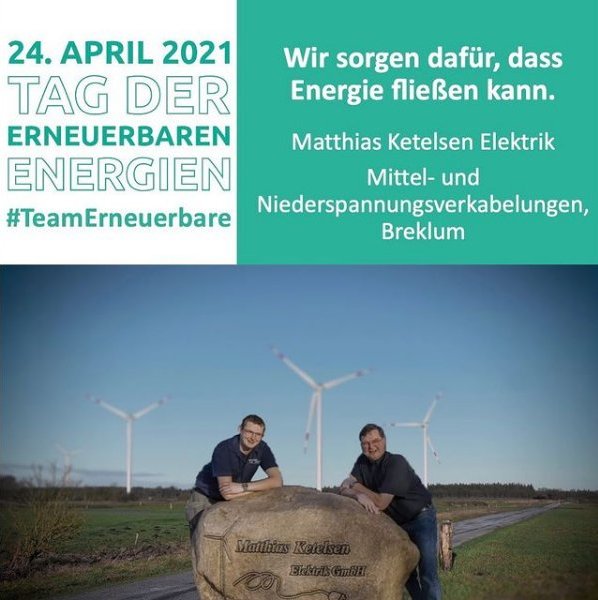 Zwei Männer stehen hinter einem großen Stein vor einem Windpark