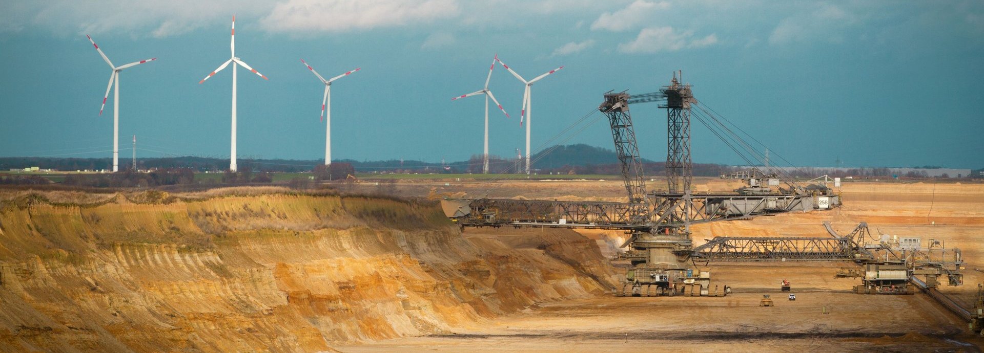 Kohlegrube mit Bohrkran. Im Hintergrund mehrere Windräder.