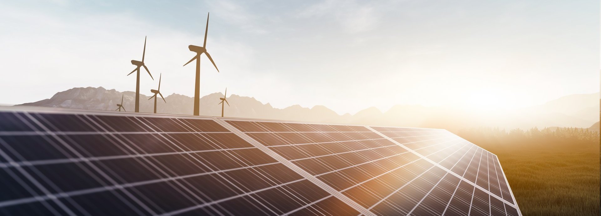 Solarkollektoren und Windräder bei Sonnenaufgang auf einem Feld mit Bergen im Hintergrund