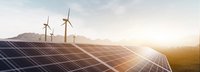 Solarkollektoren und Windräder bei Sonnenaufgang auf einem Feld mit Bergen im Hintergrund