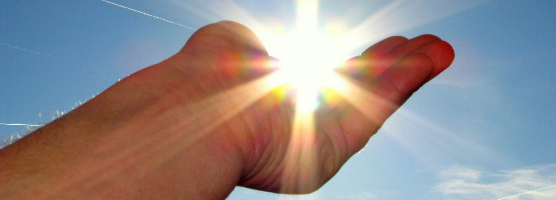 Hand hält die scheinende Sonne im Himmel in der Handfläche
