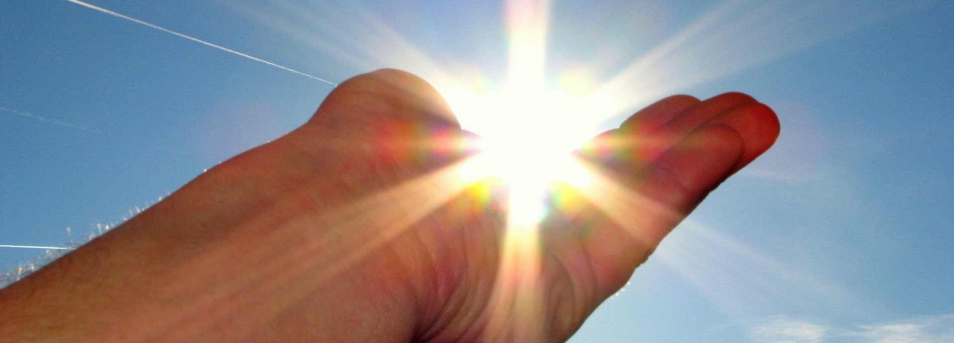 Hand hält die scheinende Sonne im Himmel in der Handfläche