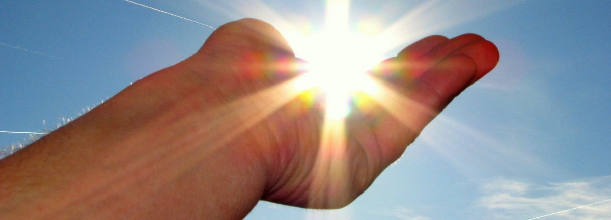 Hand hält die scheinende Sonne im Himmel in der Handfläche