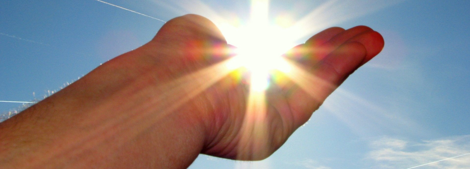 Hand hält die scheinende Sonne im Himmel in der Handfläche