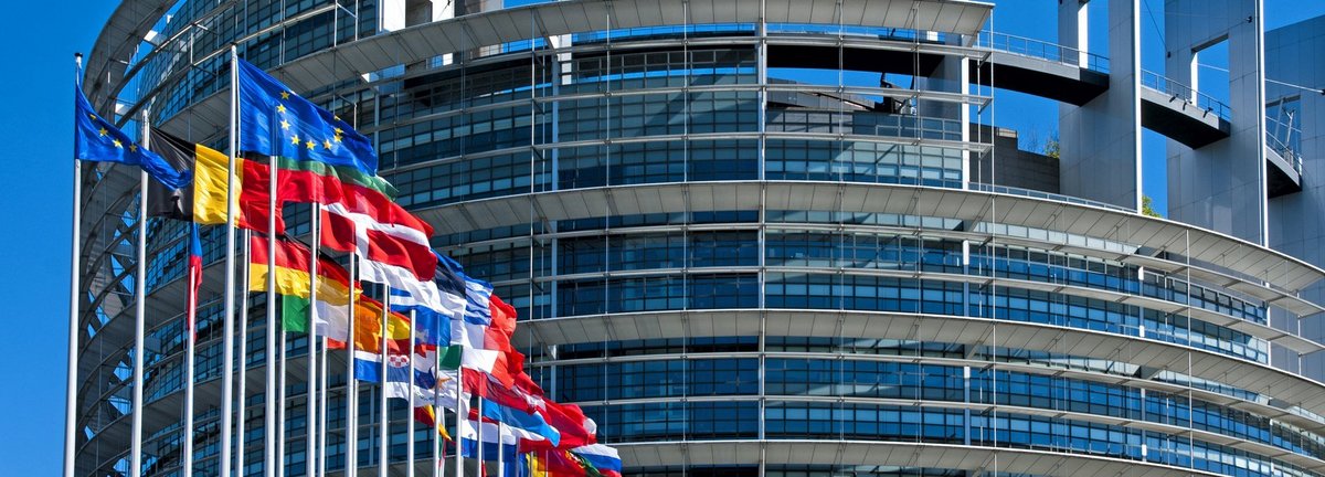 EU Parlamentsgebäude mit europäischen Flaggen vor blauem wolkenfreiem Himmel