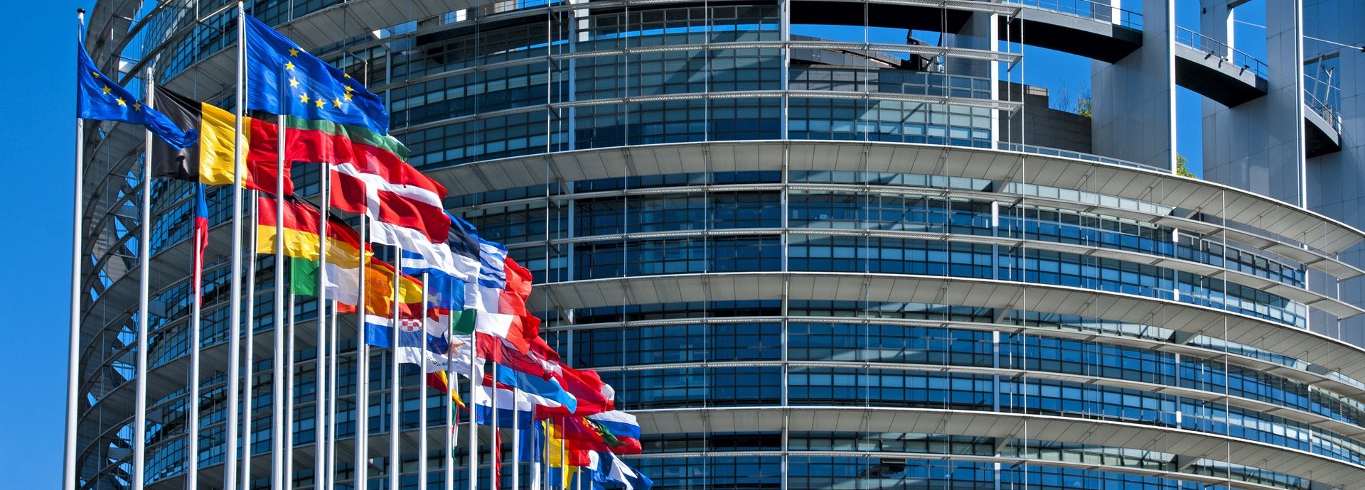 EU Parlamentsgebäude mit europäischen Flaggen vor blauem wolkenfreiem Himmel