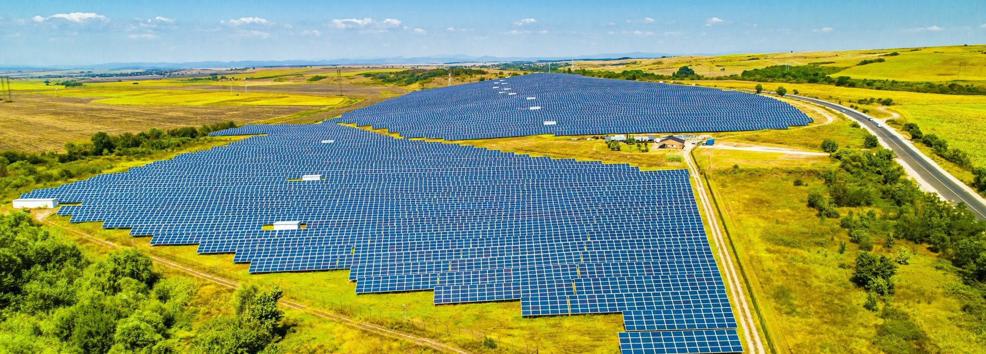 Fernaufnahme eines Solarkollektoren-Felds umgeben von Wiese und Bäumen