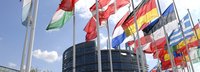 Europäisches Parlamentsgebäude im Hintergrund mit Flaggen der mitgliedsstaaten im Vordergrund vor blauem Himmel