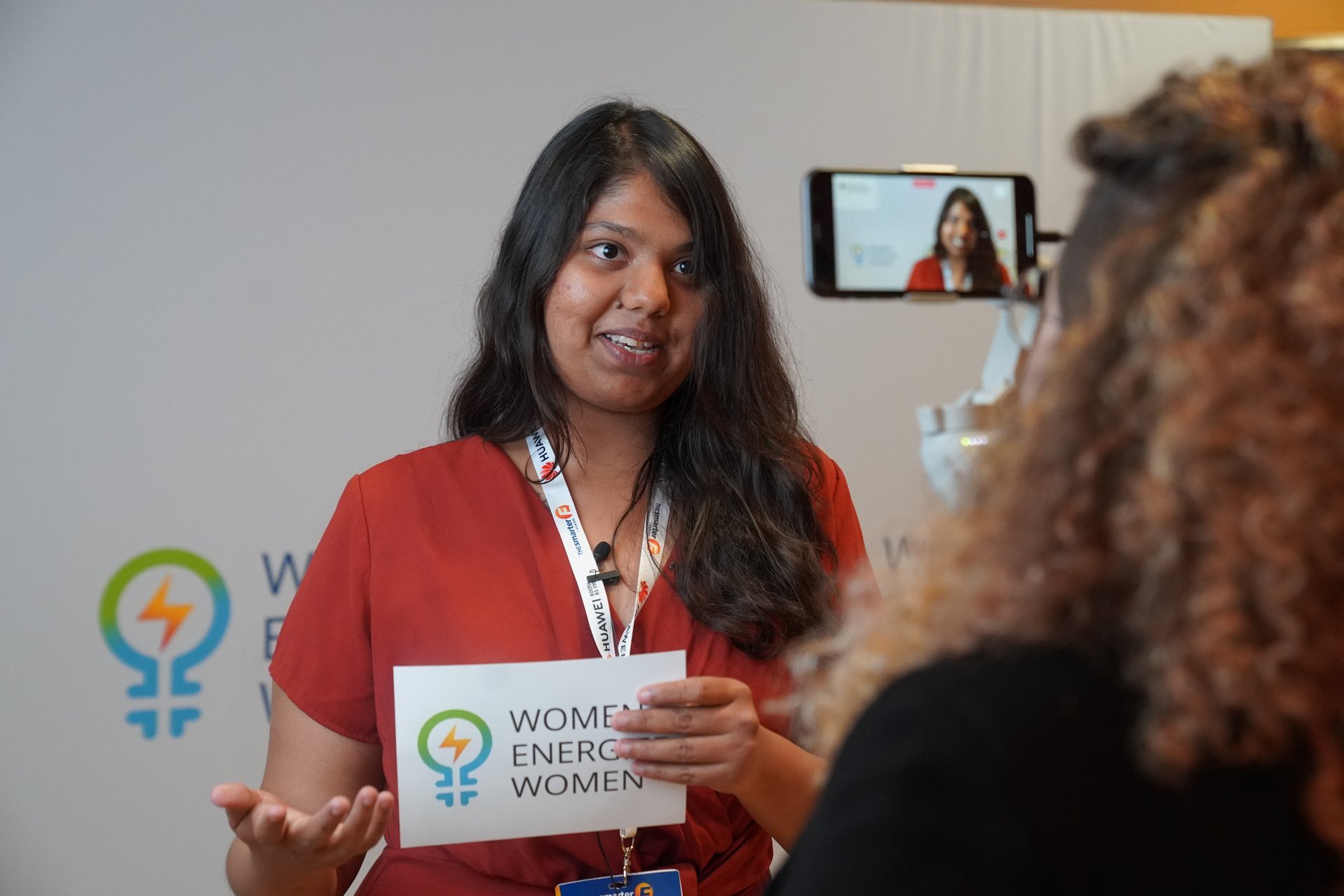 Frau hält ein Women Energize Women Schild in der Hand und wird gefilmt