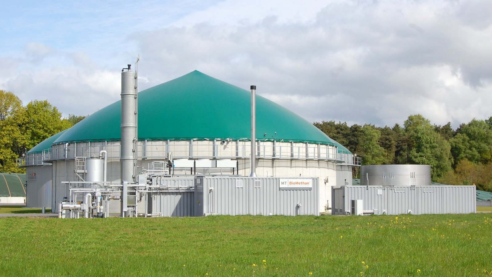 Biogasanlage mit grünem Dach auf einer Wiese und mit Bäumen im Hintergrund