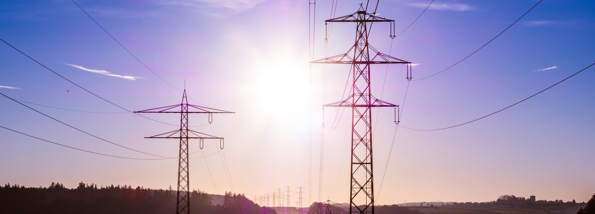 Stromtrasse vor dunkelblauem Hintergrund und Sonne auf einem nebligen Feld
