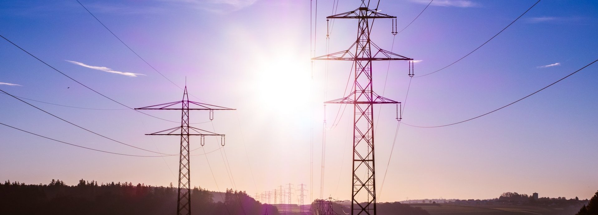 Beschreibung: Stromtrasse vor dunkelblauem Hintergrund und Sonne auf einem nebligen Feld