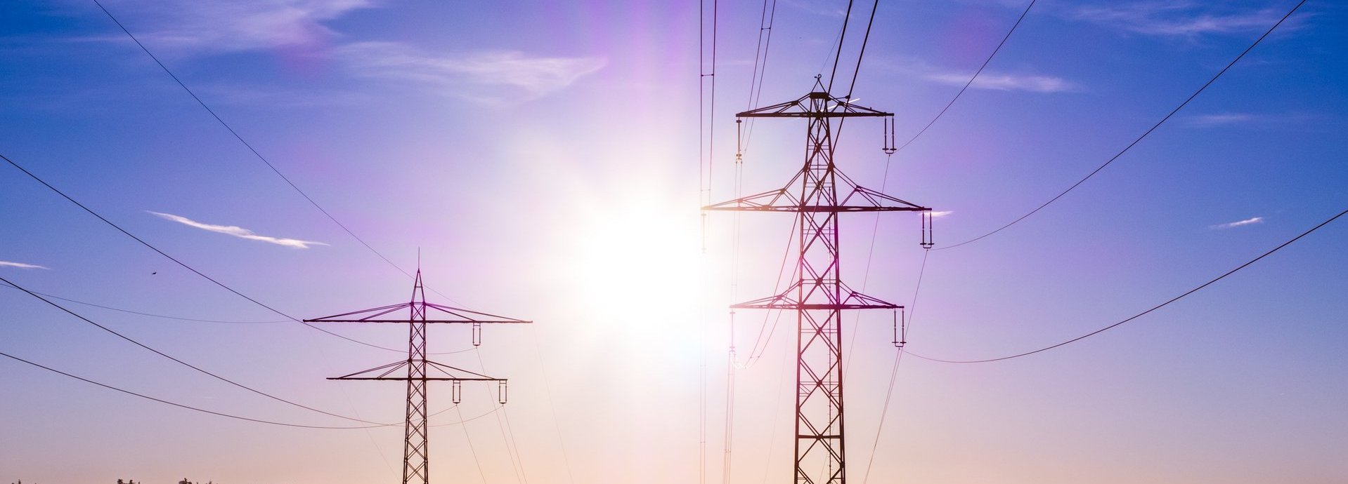 Stromtrasse vor dunkelblauem Hintergrund und Sonne auf einem nebligen Feld