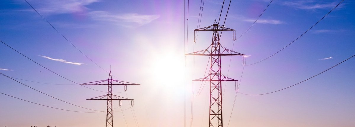 Bildbeschreibung: Stromtrasse vor dunkelblauem Hintergrund und Sonne auf einem nebligen Feld