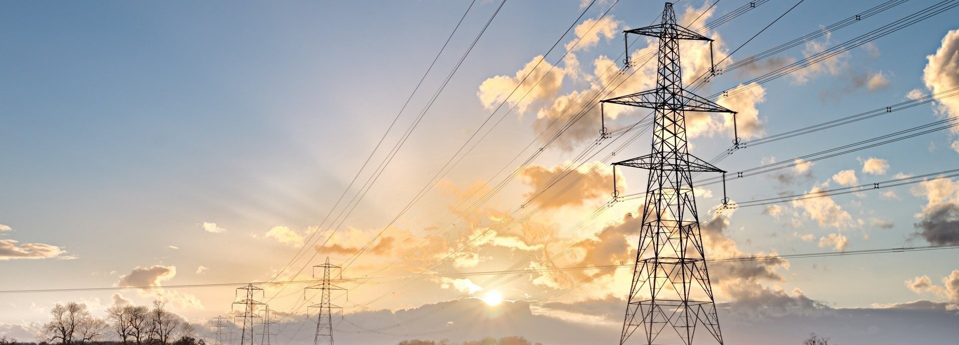 Beschreibung: Stromtrasse auf einem grünen Feld bei Sonnenaufgang