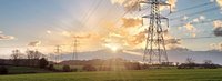 Stromtrasse auf einem grünen Feld bei Sonnenaufgang