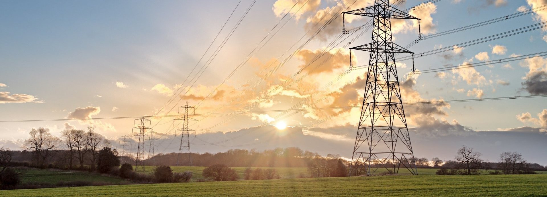 Stromtrasse auf einem grünen Feld bei Sonnenaufgang