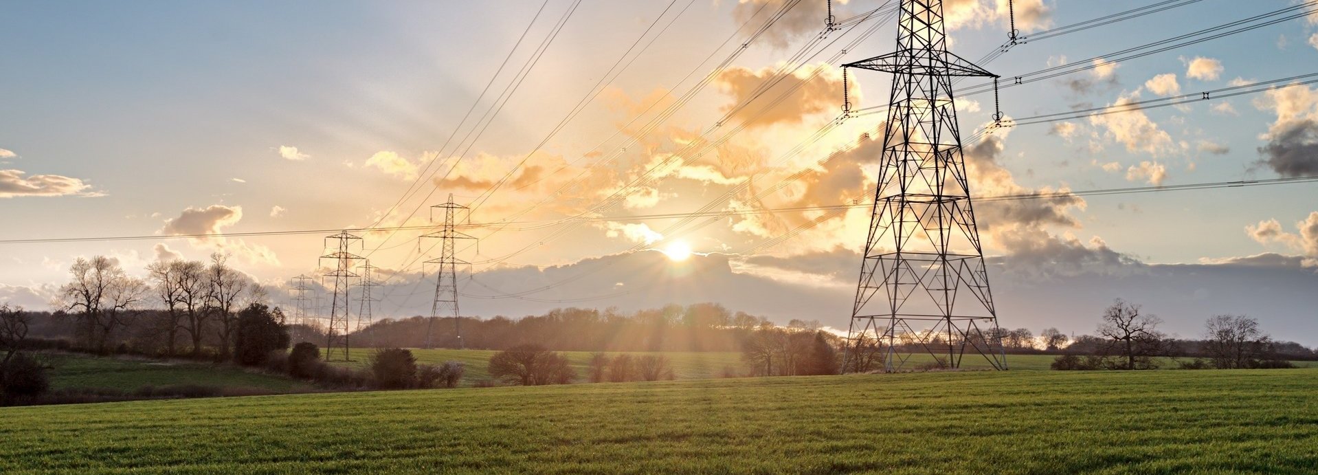 Stromtrasse auf einem grünen Feld bei Sonnenaufgang