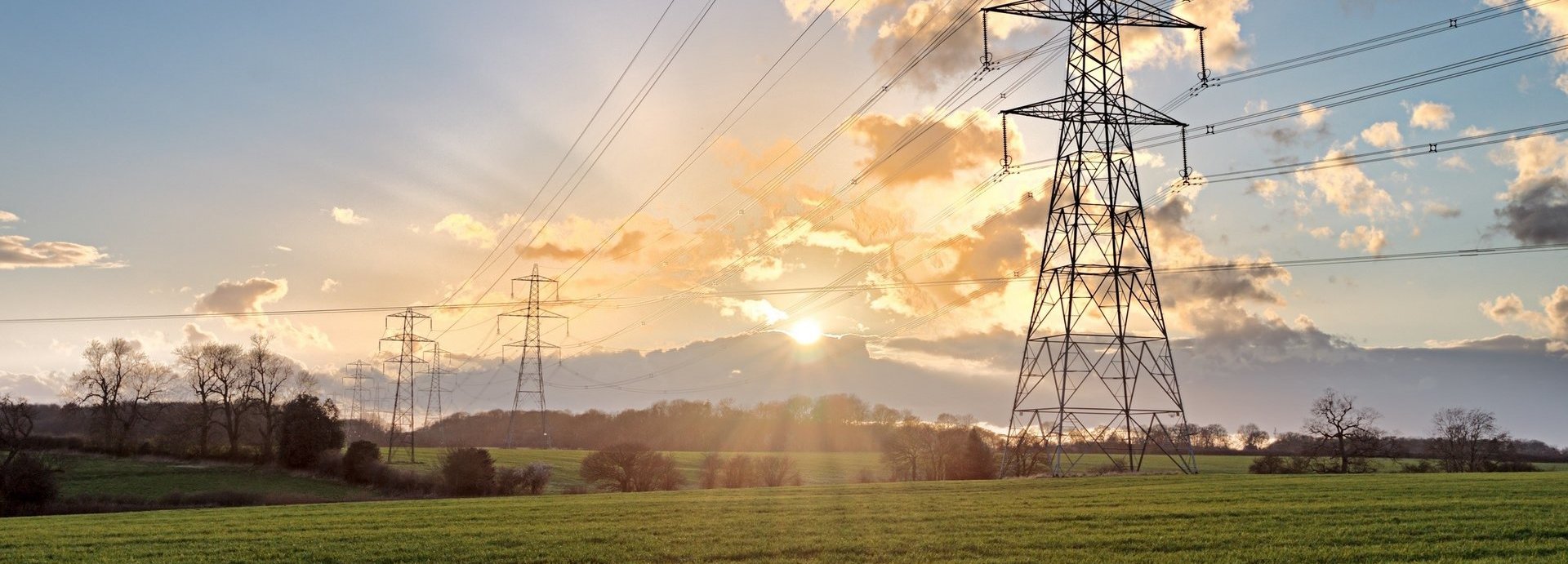 Stromtrasse auf einem grünen Feld bei Sonnenaufgang