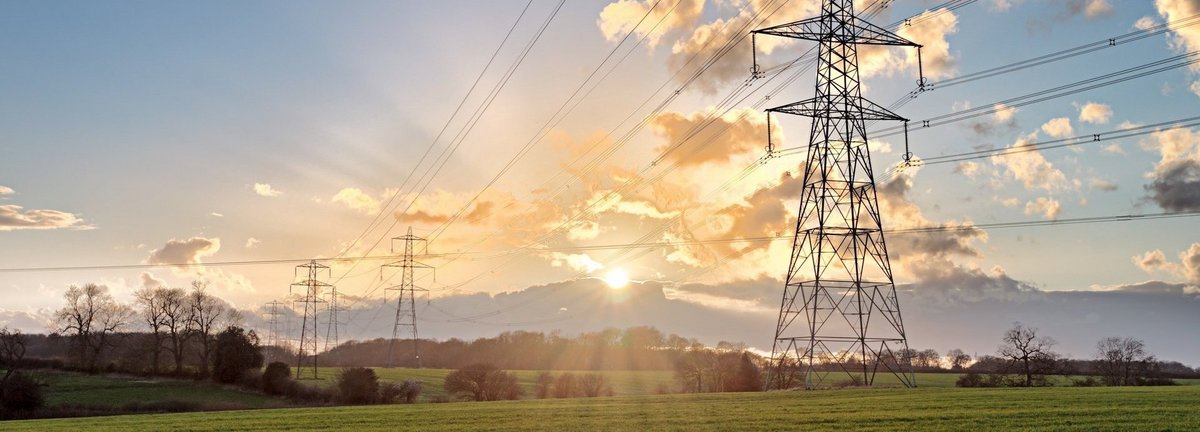 Stromtrasse auf einem grünen Feld bei Sonnenaufgang