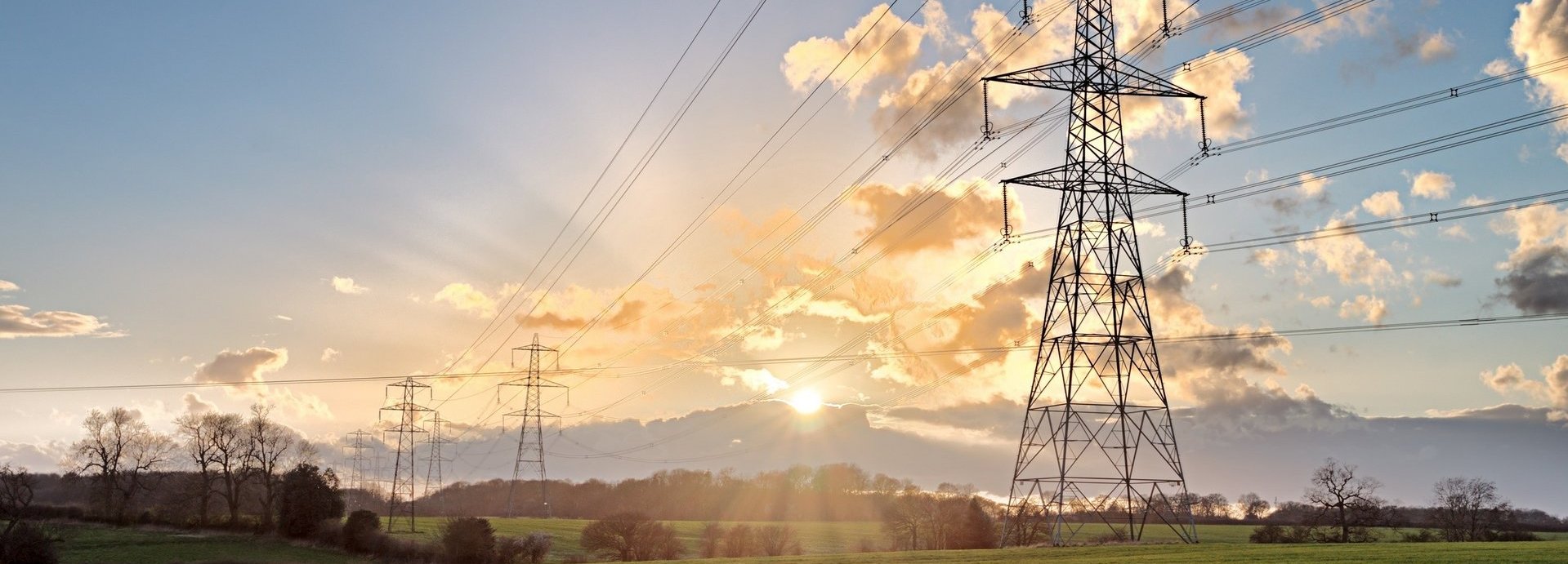 Stromtrasse auf einem grünen Feld bei Sonnenaufgang