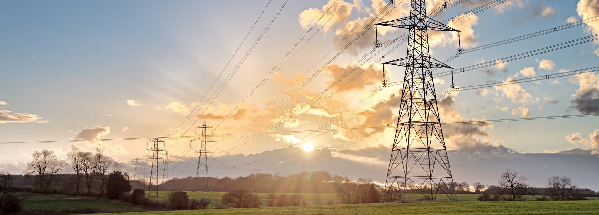 Stromtrasse auf einem grünen Feld bei Sonnenaufgang