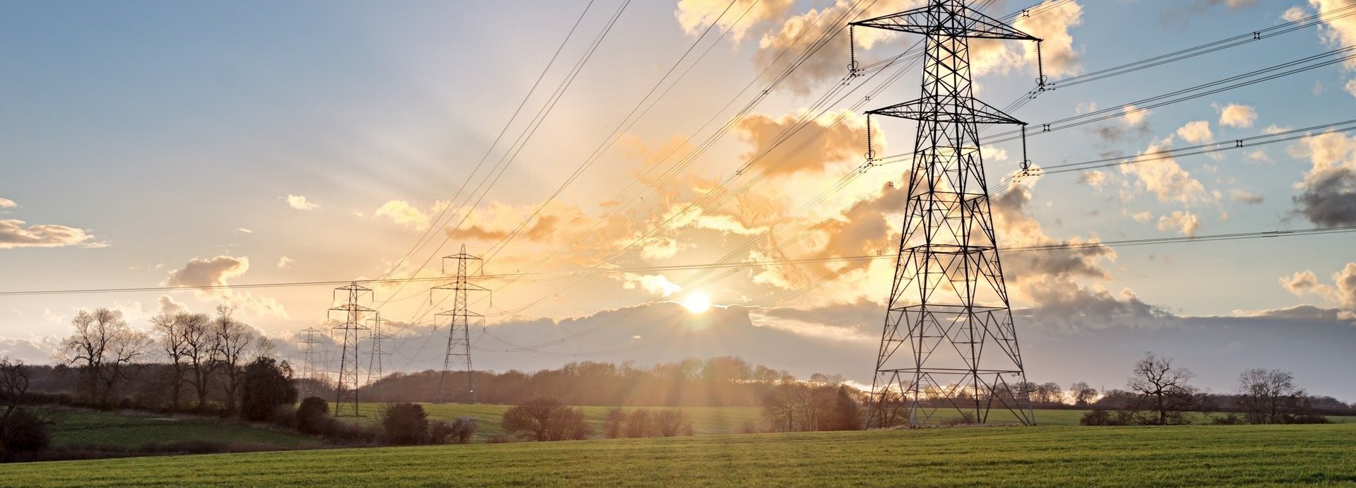 Stromtrasse auf einem grünen Feld bei Sonnenaufgang