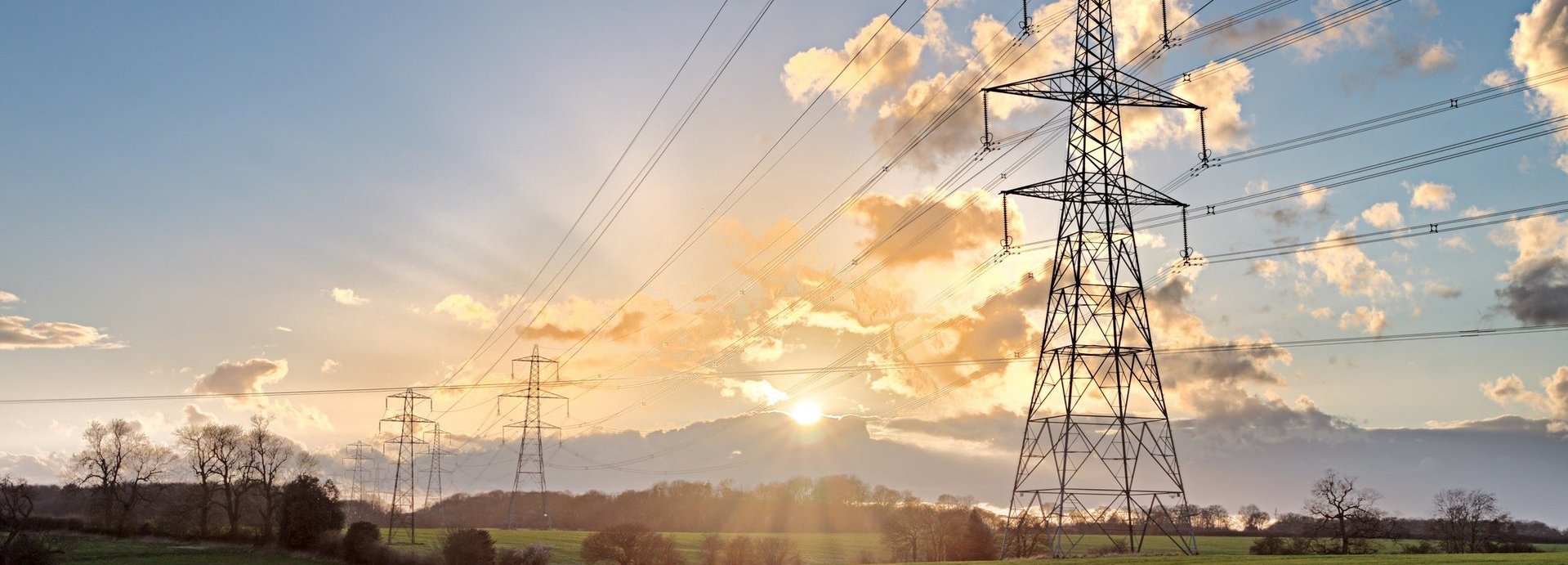 Stromtrasse auf einem grünen Feld bei Sonnenaufgang