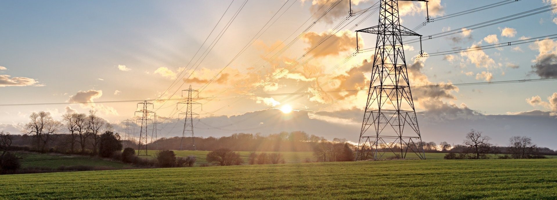 Stromtrasse auf einem grünen Feld bei Sonnenaufgang