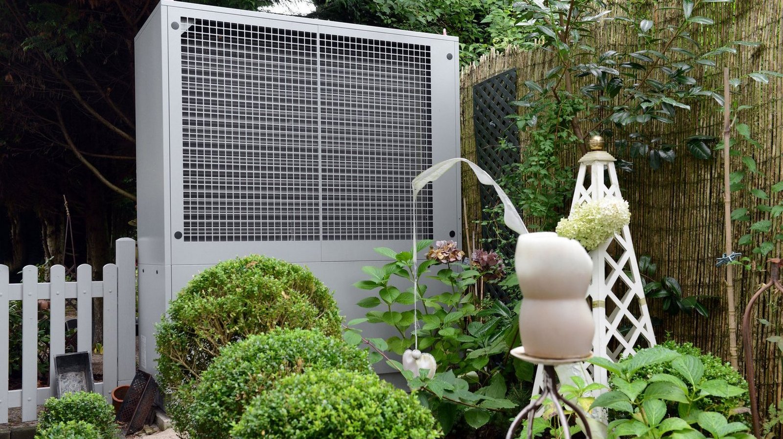 Weiße Wärmepumpe in einem grünen Garten mit Dekor