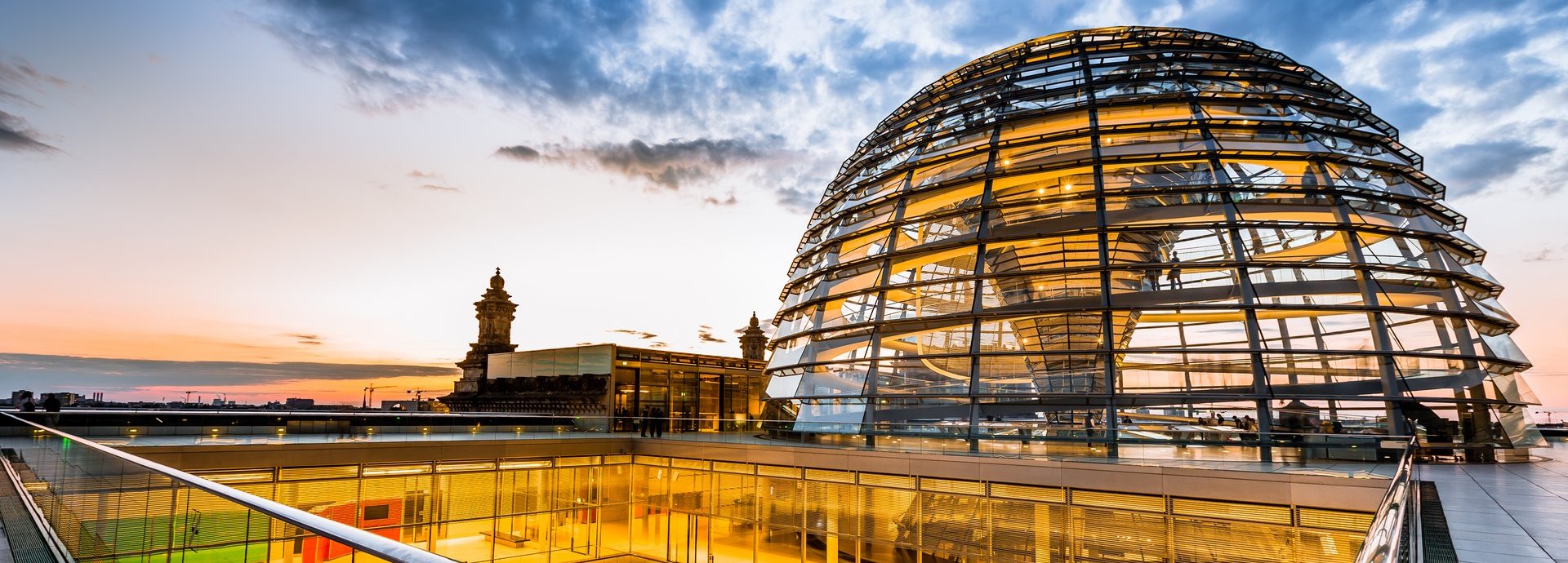 Gelb beleuchtete Kuppel und innere Gänge des Bundestags vor dunkelblauem wolkigem Himmel