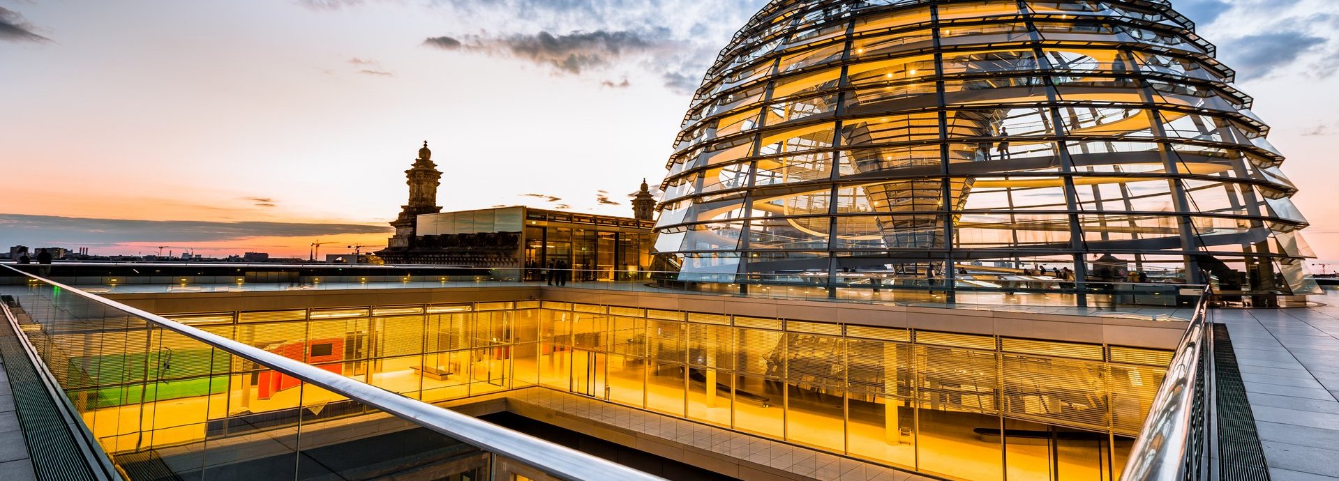 Beschreibung: Gelb beleuchtete Kuppel und innere Gänge des Bundestags vor dunkelblauem wolkigem Himmel