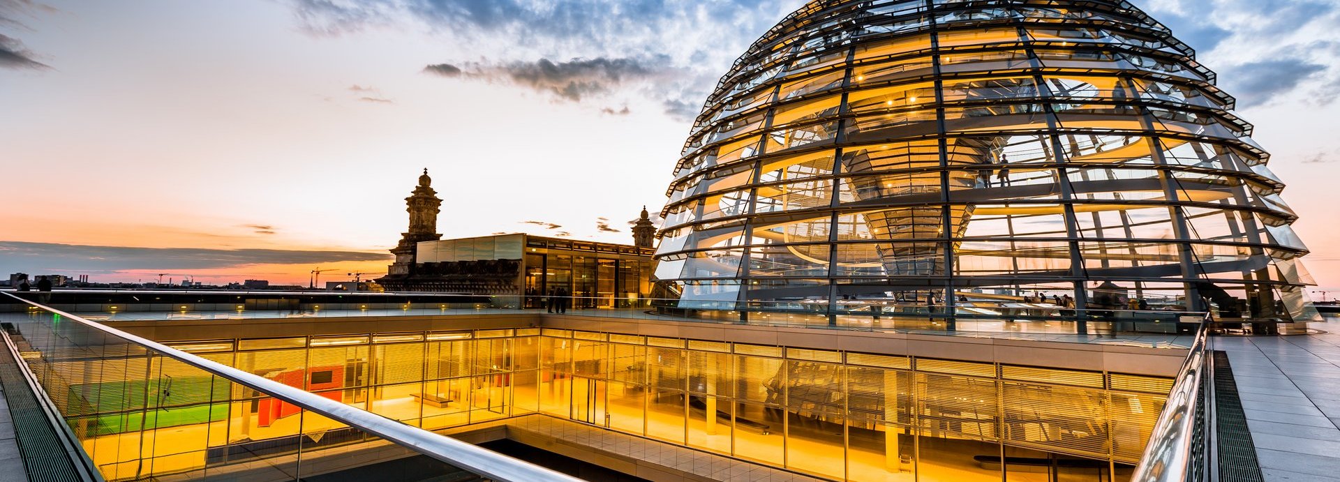 Gelb beleuchtete Kuppel und innere Gänge des Bundestags vor dunkelblauem wolkigem Himmel